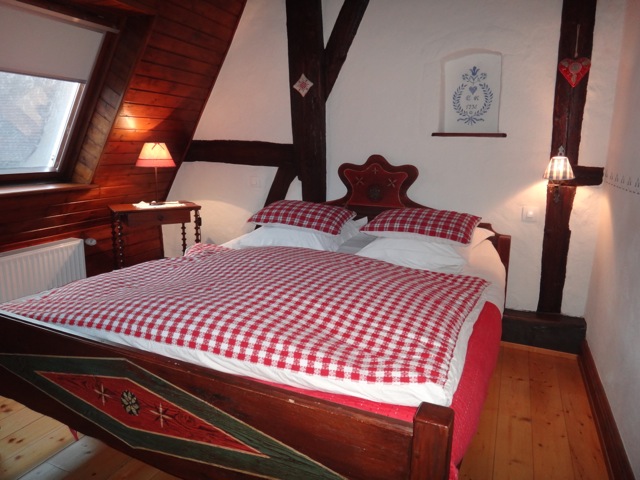 La chambre du grenier, son lit à carreaux rouges sous les poutres