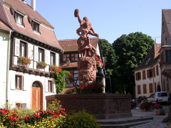 La fontaine sculptée de la place, entourée de fleurs